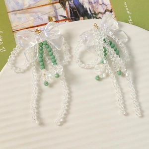 Détail de boucles d'oreilles à pampilles avec nœuds irisés et perles vertes dépolies sur un plat