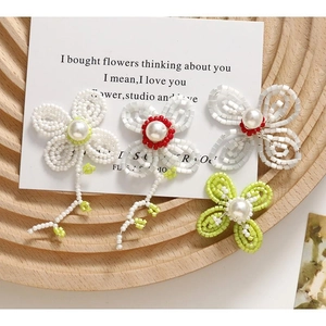 Detail of handcrafted woven flower earrings with large pearls and green bead accents