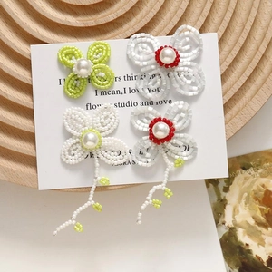 Handmade beaded flower earrings with pearls and tassels displayed on a wooden tray
