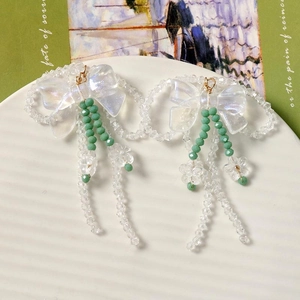 Boucles d'oreilles nœud irisées avec perles vertes et fleurs en acrylique sur un plateau