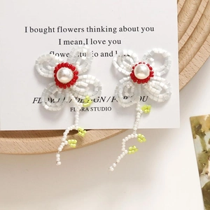 Close-up of handmade white beaded flower earrings with pearl centers on an aesthetic card
