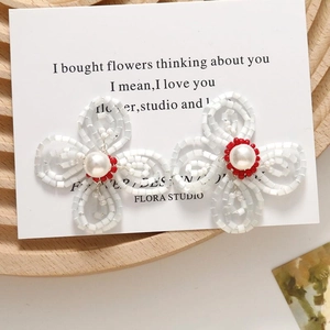 Detailed view of handmade beaded flower earrings with white pearls on a wood tray