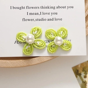 Close-up of handmade green beaded flower earrings with a white pearl center on a wooden tray