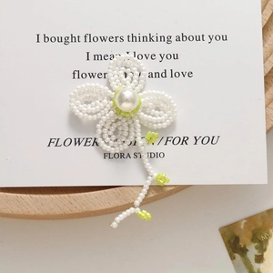 Detail of handmade pearl flower earring with green bead accents and tassels