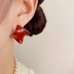 Detailed view of red glossy geometric earrings featuring a twisted square design on model