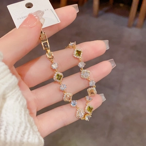 Détail d'un bracelet doré avec des zircons colorés et une étiquette montrant la qualité