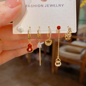 Detail of red gourd earrings set with pearls and gold chains in hand display