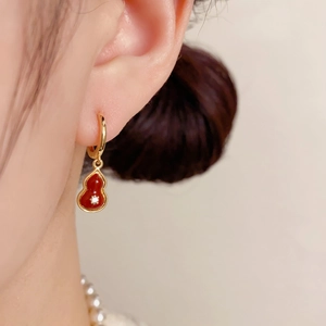 Detailed view of gold wulu earrings with red enamel inlay on a model ear