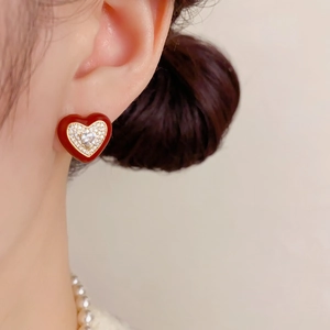 Détail de boucles d'oreilles cœur en émail rouge avec zircons brillants sur modèle