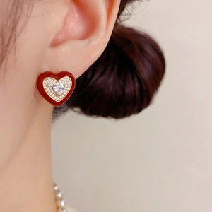 Détail d'une boucle d'oreille cœur en émail rouge avec cristaux pavés et dorure sur peau