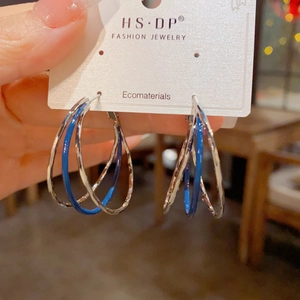 Detail of triple-layer textured silver hoop earrings with blue enamel on a brand card