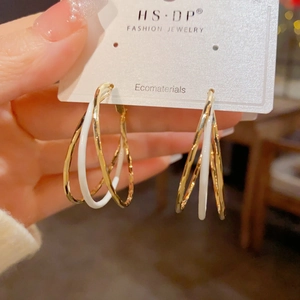 Detailed view of layered gold textured hoops and white enamel ring on a display card