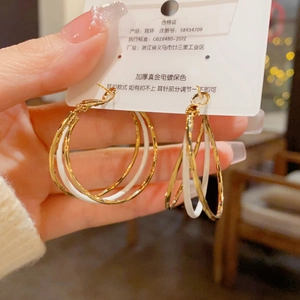 Close-up of triple-layered gold-plated hoop earrings with white enamel finish