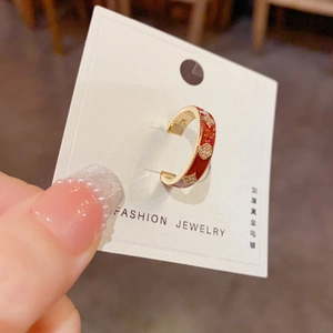 Détail macro d'une bague ouverte dorée avec émail rouge et motif trèfle en diamant