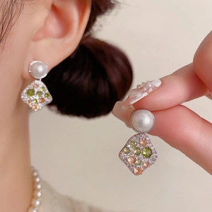Detail of elegant geometric drop earrings with white pearls and multicolor cubic zirconia