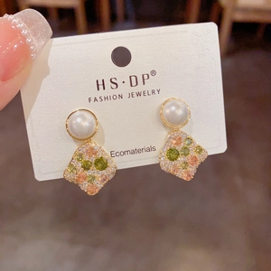 Detailed macro view of gold-tone geometric earrings with zircon inlay and pearl accent