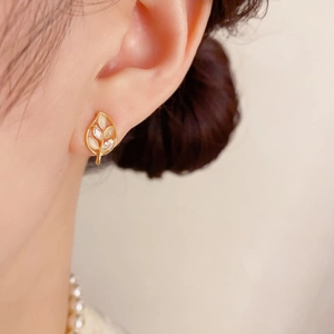 Detailed close-up of gold leaf-shaped earrings with pearls and crystals on a model