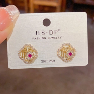 Detalle de pendientes Fu dorados con halo de circonitas y piedra roja central