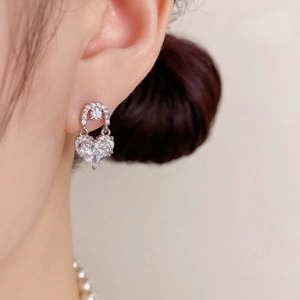 Detail of silver heart earring with zircon stones worn by a model with pearl necklace