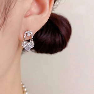 Elegant silver-toned heart drop earrings with shimmering crystals on a female model