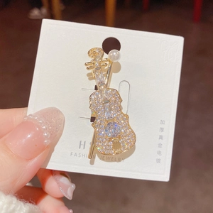 Detailed close-up of a gold-plated violin brooch with crystals and a white pearl