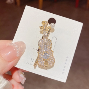 Detailed close-up of a golden violin brooch featuring white cubic zirconia and a pearl