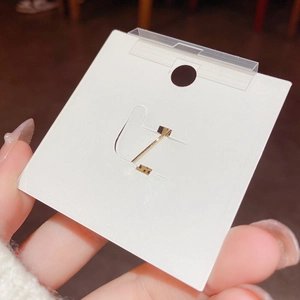 Minimalist small gold hoop earrings displayed on a white jewelry card holder