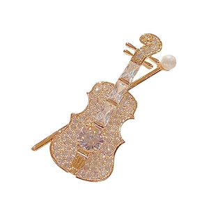 Elegant gold violin brooch with sparkling crystals and pearl detail on white background