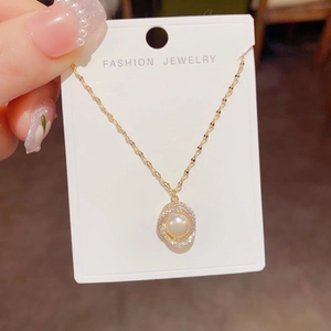 Detail of gold necklace with zircon paved rings and white pearl pendant on card