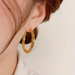 Détail de grandes créoles dorées avec texture grainée portées par un mannequin