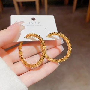 Détail de boucles d'oreilles créoles dorées avec texture métallique sur carte blanche