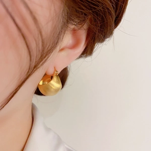 Nahaufnahme goldener, gebürsteter C-Ohrringe am Modell im minimalistischen modernen Stil