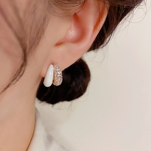 Elegant gold earrings with white resin half-sphere and micro-set crystals worn on ear
