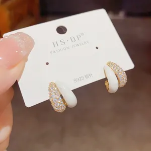 Detailed close-up of C-shaped earrings with pave-set zircons and white enamel finish
