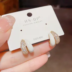 Detailed close-up of gold-plated hoop earrings with micro-set zircons and white enamel