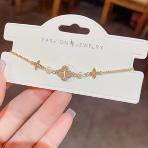 Detailed close-up of a gold-plated bracelet with four-leaf clover, pearls and crystals