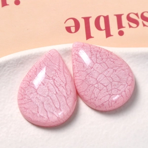 Detail of pink resin teardrop charms with smoky crackle texture on a white tray