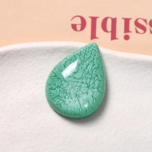 Macro shot of mint green teardrop resin charm with detailed dark crackle texture