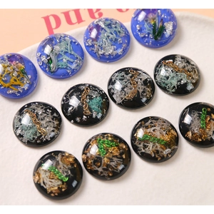 Dettaglio macro di cabochon in resina con catene in metallo, foglia oro e fiori essiccati