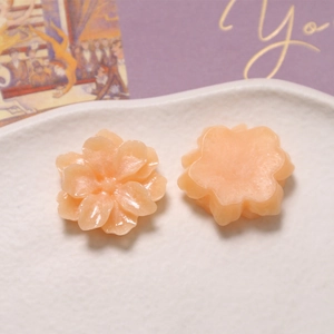 Detailed peach resin gardenia flower charms displayed on a textured white ceramic tray