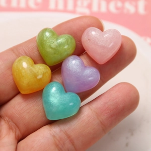 Close-up of glittery resin heart charms in pastel colors held in palm for scale
