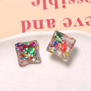 Macro detail of square resin charms with colorful iridescent flakes on ceramic plate