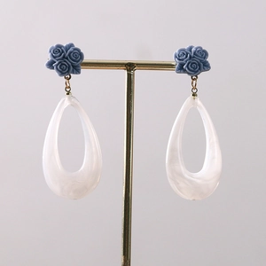 Macro detail of blue resin rose earrings with white teardrop pendants on a gold T-stand
