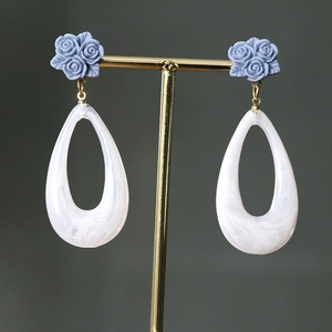 Detail of blue rose stud earrings with white marble resin teardrop pendants on gold stand