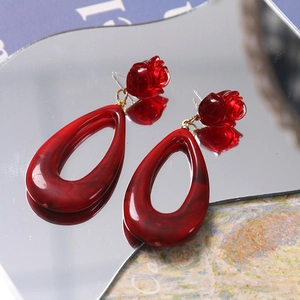 Macro shot of red resin rose earrings with marbled teardrop pendants on a mirror surface