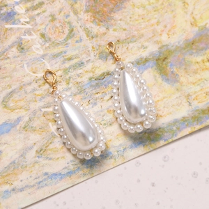 Detailed view of teardrop pearl charms with gold wire wrap on artistic background