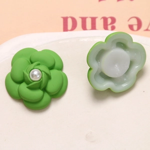 Detail view of green camellia flower charm with pearl center and back plastic buckle