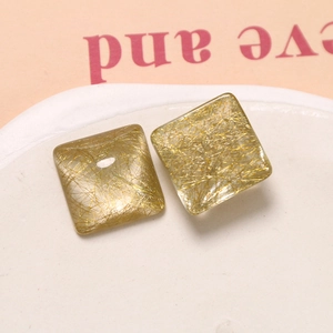 Detailed macro view of square resin charms with silk-like gold fibers for DIY jewelry
