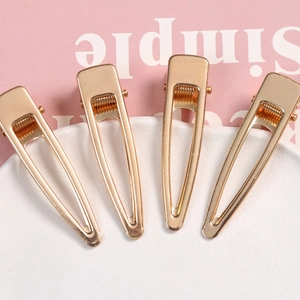 Close-up of four golden alloy geometric duckbill hair clips on a white ceramic tray