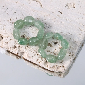 Detail view of green natural stone beaded rings with oval gems on white travertine